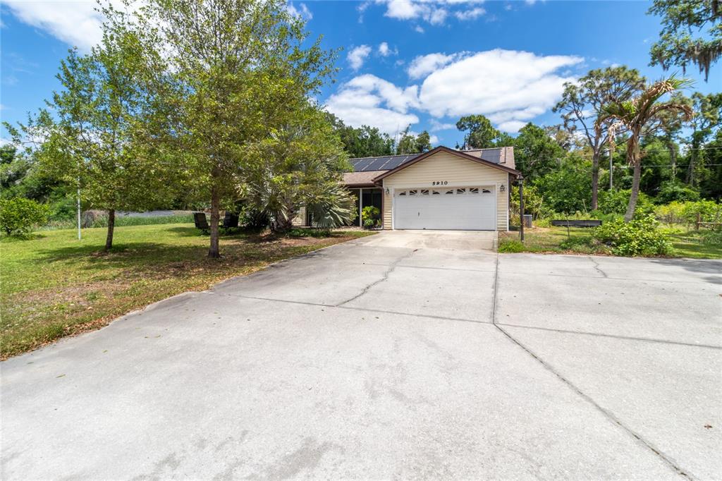 A single-story house with a concrete driveway, solar panels on the roof, and surrounding trees — 5910 BELLA ROAD, PARRISH, FL