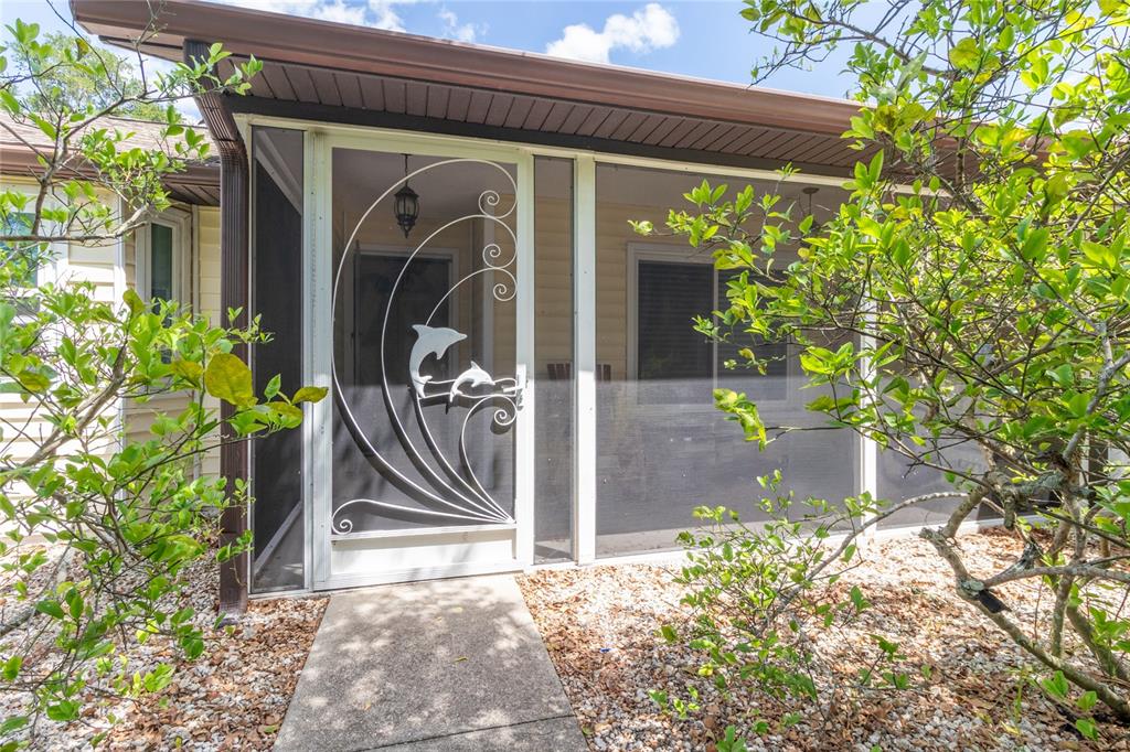 A screened-in porch features a white metal storm door with a dolphin design — 5910 BELLA ROAD, PARRISH, FL