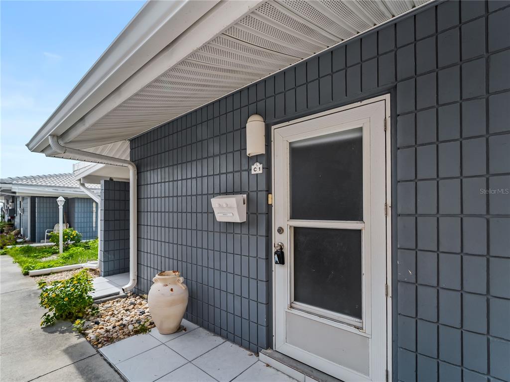 A gray tiled exterior wall features a white door, a mailbox, and a decorative vase — 1205 TARPON CENTER DRIVE UNIT C1, VENICE, FL