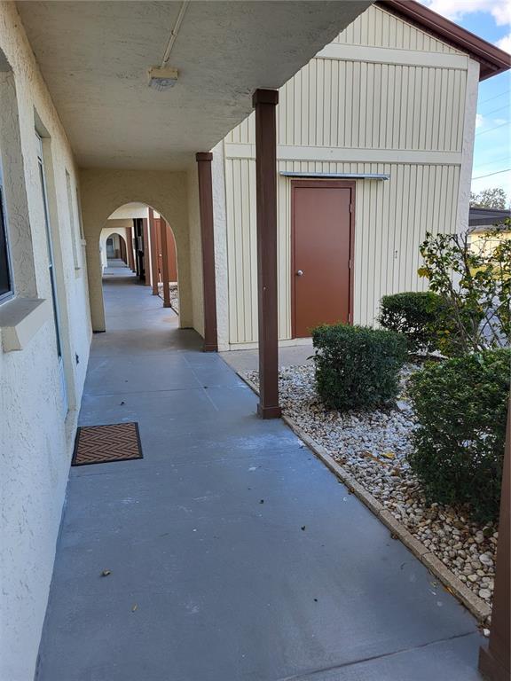 A covered walkway with arched supports leads past a tan building with a brown door — 4956 HARBOR VILLA LANE UNIT 103, NEW PORT RICHEY, FL