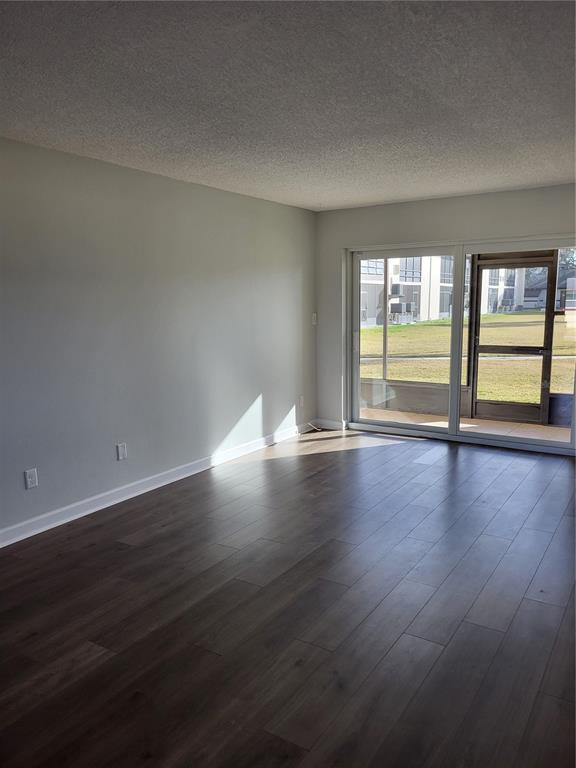 An empty living room with dark wood flooring, light gray walls, and a sliding glass door — 4956 HARBOR VILLA LANE UNIT 103, NEW PORT RICHEY, FL