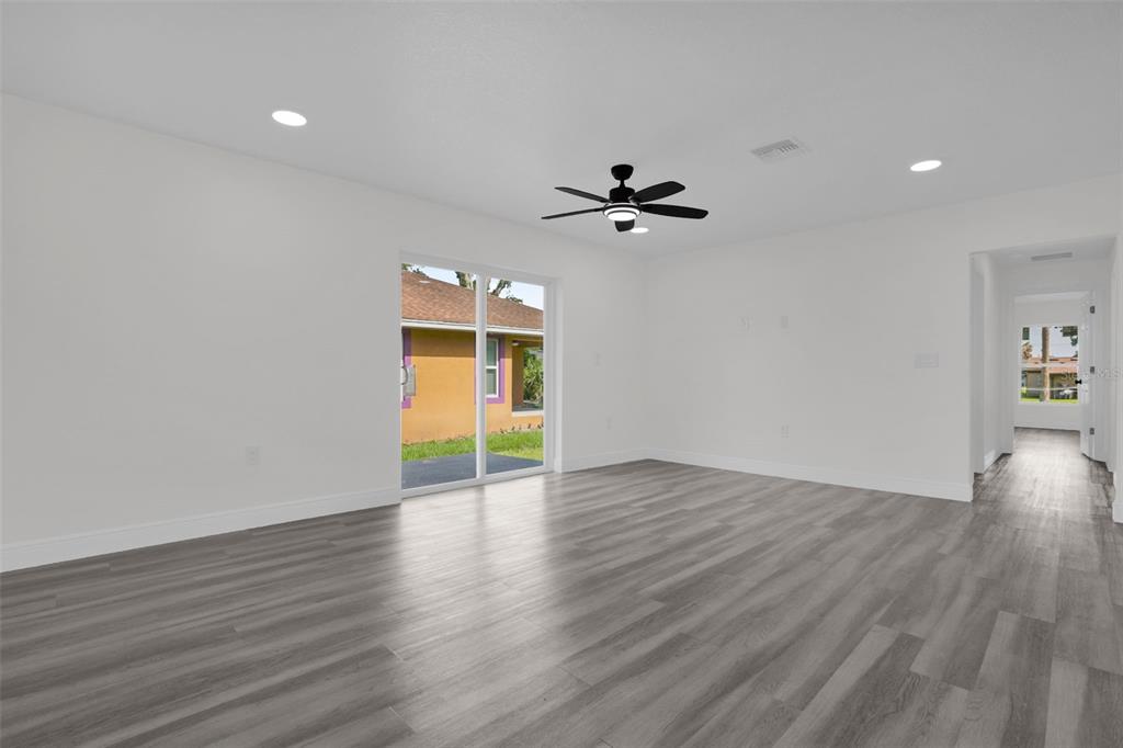 A bright, empty room features white walls, gray wood-look flooring, a ceiling fan, and sliding doors — 1704 W 15TH STREET, SANFORD, FL