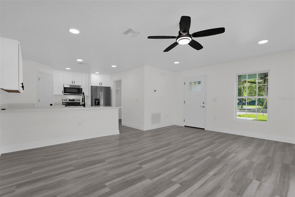 A bright, open-concept living room and kitchen area with white walls and gray wood flooring — 1704 W 15TH STREET, SANFORD, FL