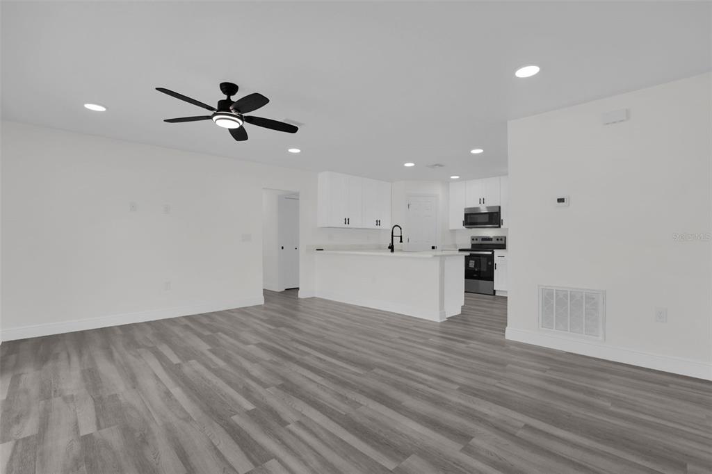 An open-concept kitchen and living area feature white cabinetry, stainless steel appliances, and wood-look flooring — 1704 W 15TH STREET, SANFORD, FL
