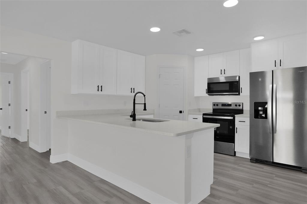 A modern kitchen features white cabinets, stainless steel appliances, and a central island with sink — 1704 W 15TH STREET, SANFORD, FL
