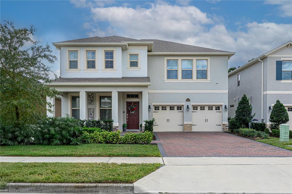 A two-story suburban house features a brick driveway, two-car garage, and a covered front porch — 18344 OLIVER TWIST WAY, WINTER GARDEN, FL