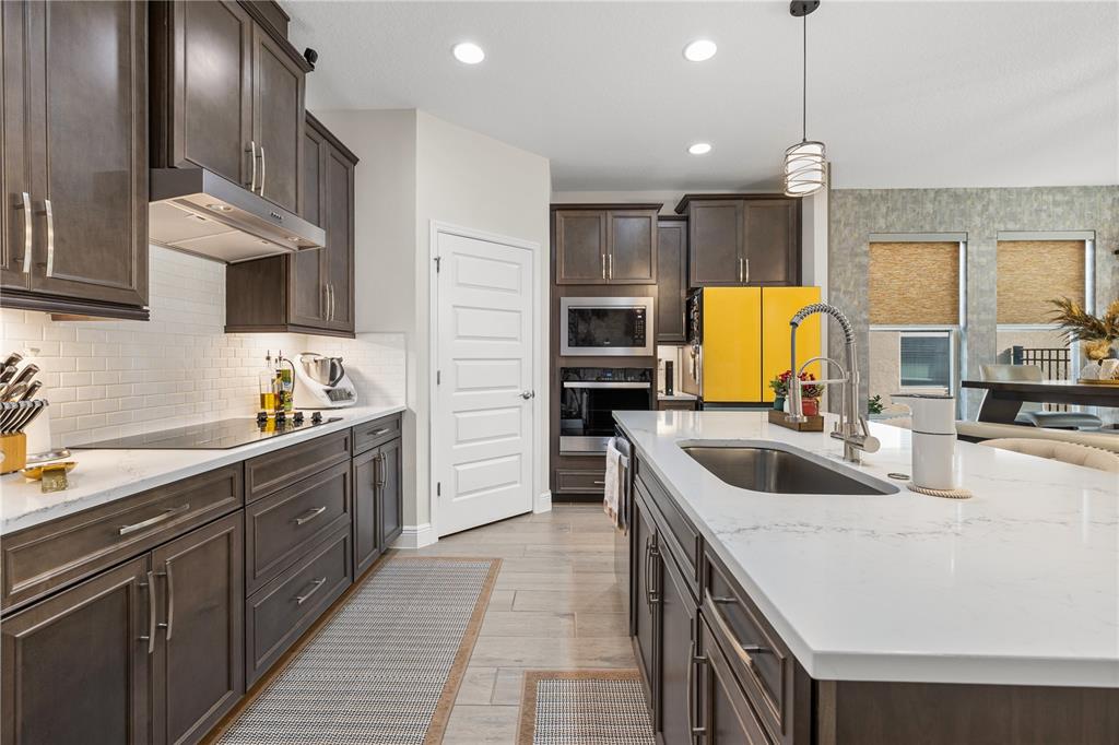 A modern kitchen features dark wood cabinets, white countertops, stainless steel appliances, and a yellow refrigerator — 18344 OLIVER TWIST WAY, WINTER GARDEN, FL