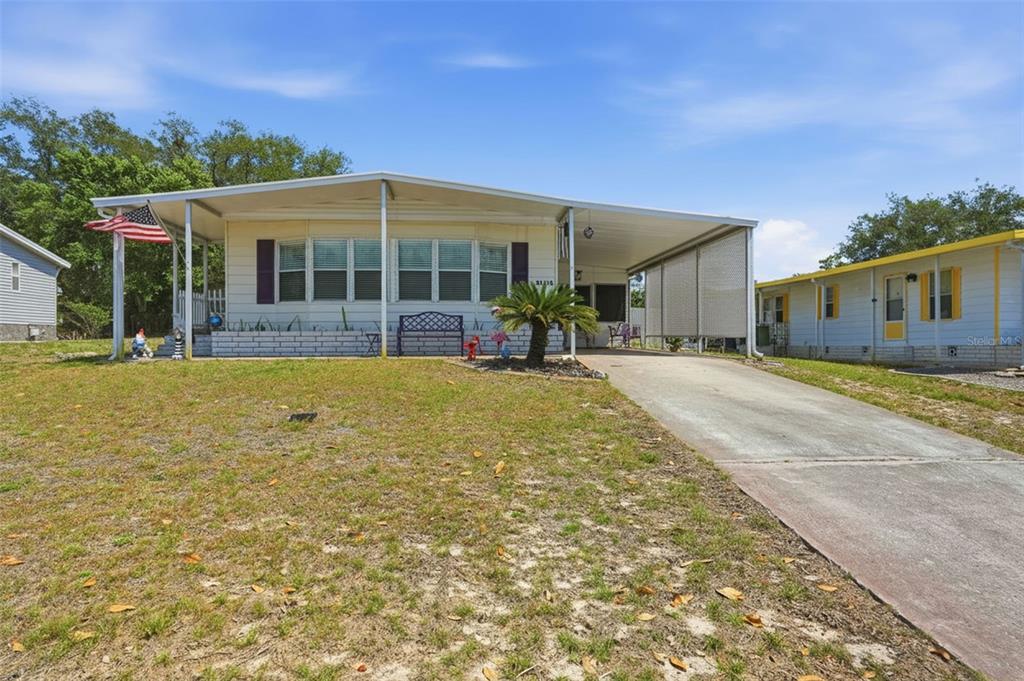 A single-story manufactured home features a front porch, a carport, and a concrete driveway — 15080 RIALTO AVENUE, BROOKSVILLE, FL
