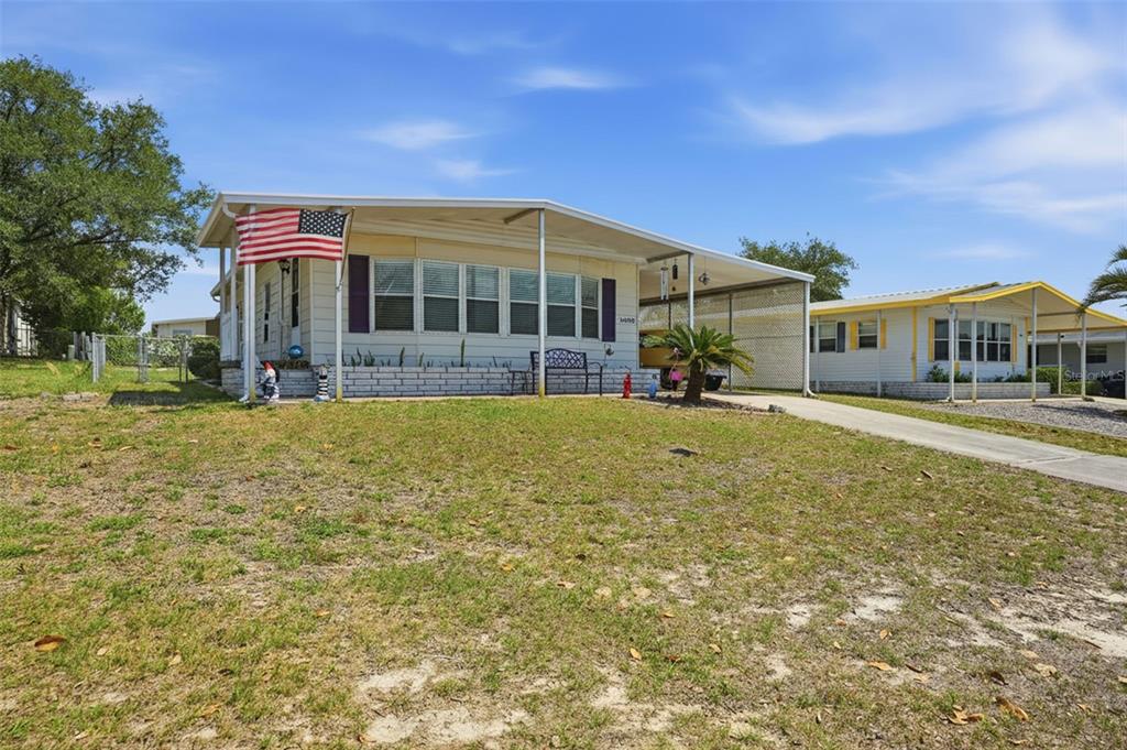 A single-story manufactured home with a front porch, carport, and American flag — 15080 RIALTO AVENUE, BROOKSVILLE, FL