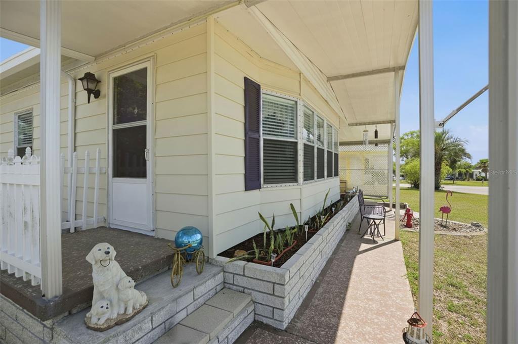 A light-colored mobile home exterior features a covered porch, a brick planter, and a dog statue — 15080 RIALTO AVENUE, BROOKSVILLE, FL