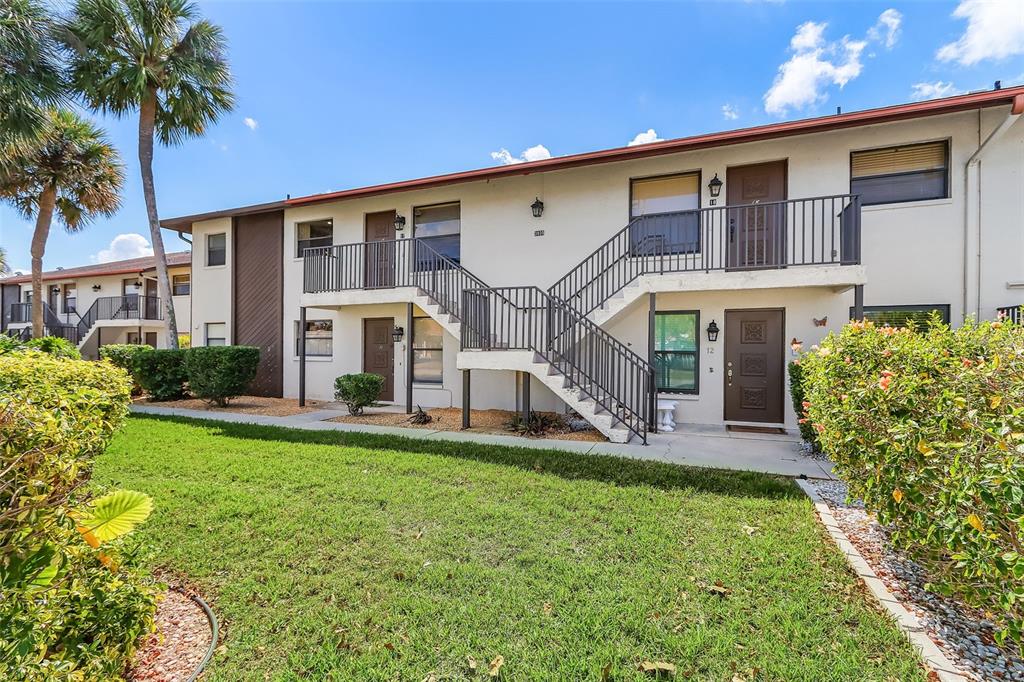 A two-story apartment building features exterior staircases, brown doors, and a landscaped front lawn — 3935 COUNTRY CLUB BOULEVARD UNIT 17, CAPE CORAL, FL