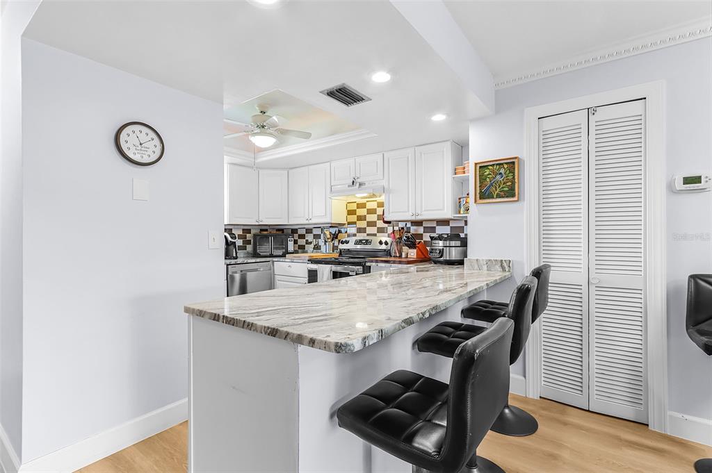 A kitchen features white cabinets, a marble-topped breakfast bar, and three black stools — 3935 COUNTRY CLUB BOULEVARD UNIT 17, CAPE CORAL, FL