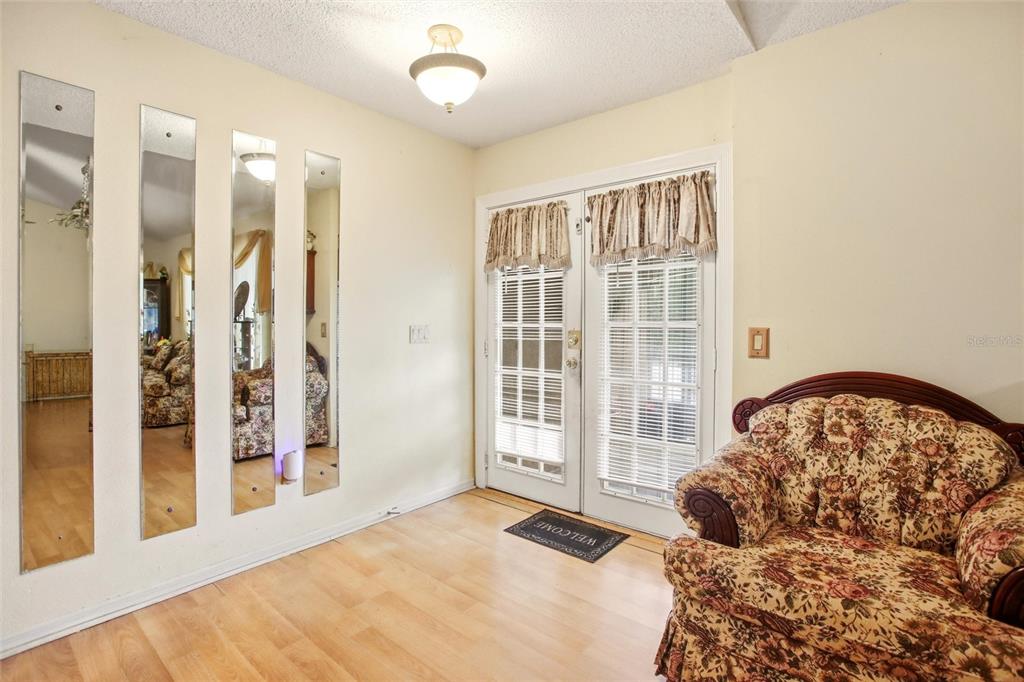 A room with light wood flooring, four vertical wall mirrors, and a floral patterned armchair — 3456 DWIGHT STREET, PORT CHARLOTTE, FL