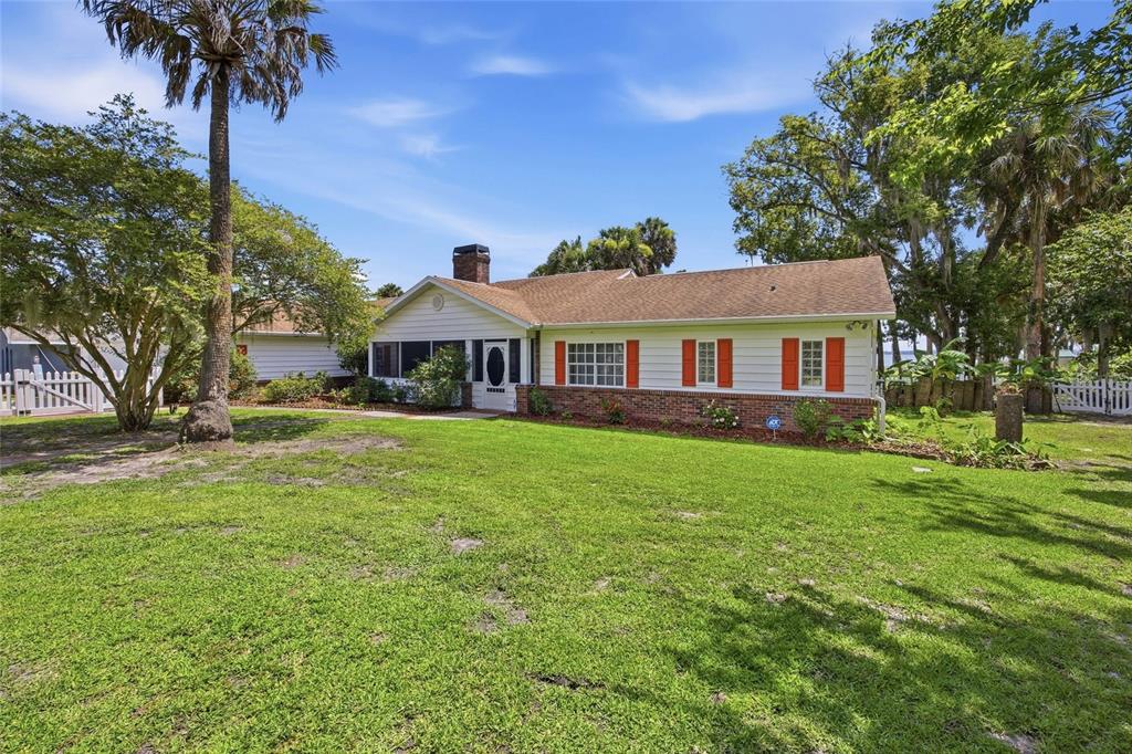 A single-story house with white siding, red shutters, a brick base, and a large lawn — 1100 N PALMETTO STREET, LEESBURG, FL
