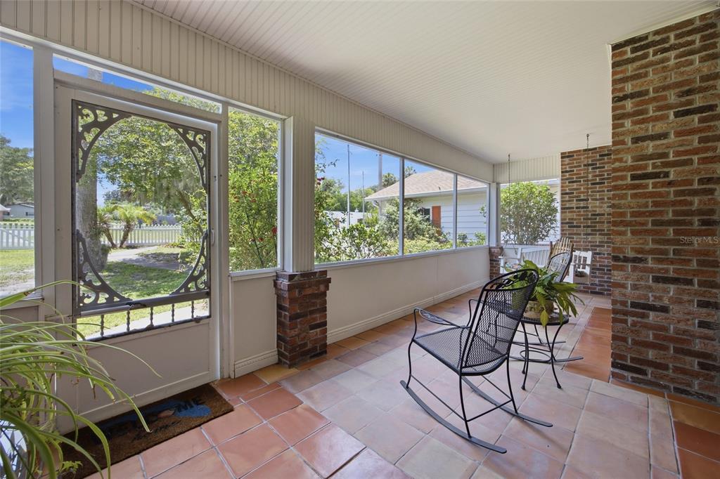 A screened-in porch features tile flooring, a brick accent wall, and a metal rocking chair — 1100 N PALMETTO STREET, LEESBURG, FL