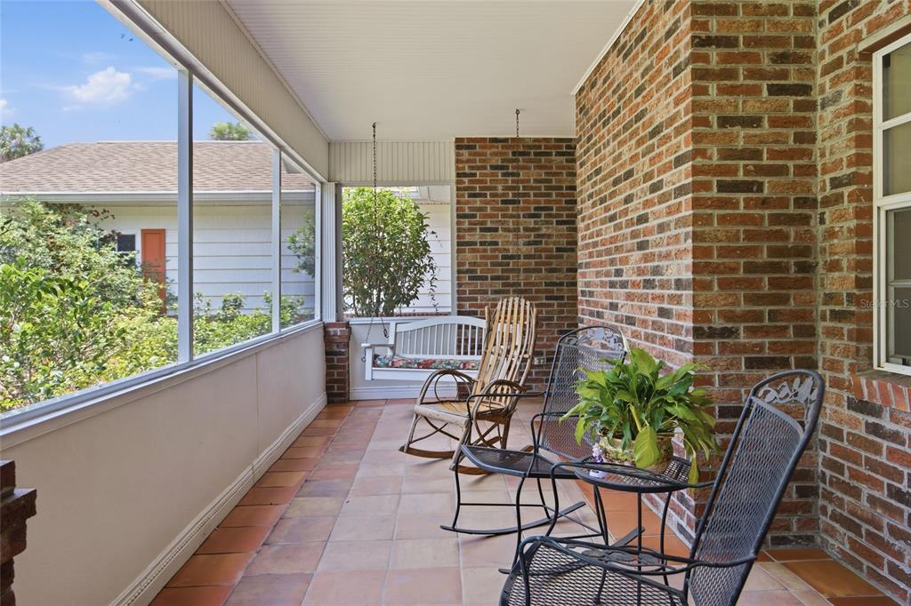 A screened-in porch features a brick wall, tile flooring, a hanging bench, and rocking chairs — 1100 N PALMETTO STREET, LEESBURG, FL
