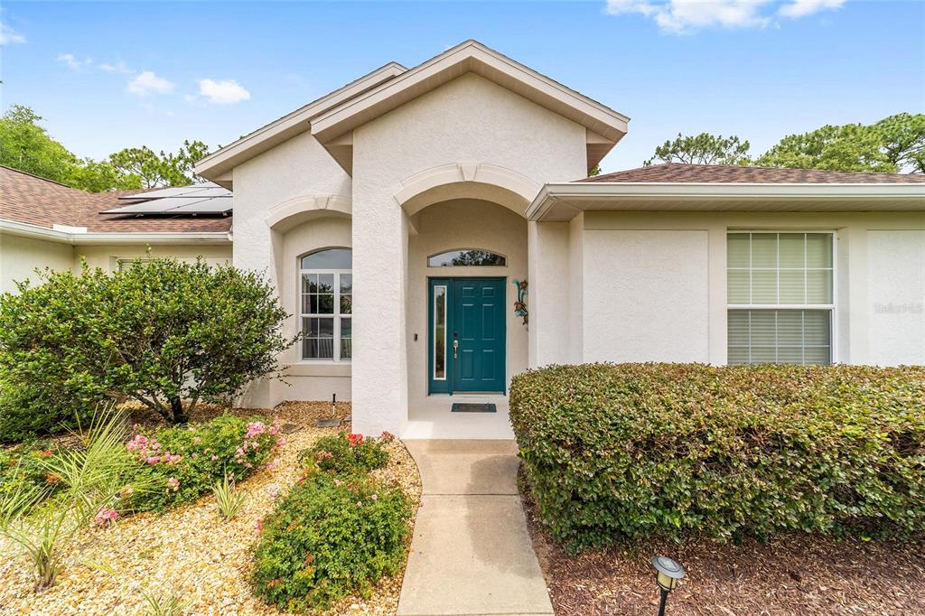 The exterior of a single-story home features a teal front door and a concrete walkway — 9781 SW 196TH CIRCLE, DUNNELLON, FL