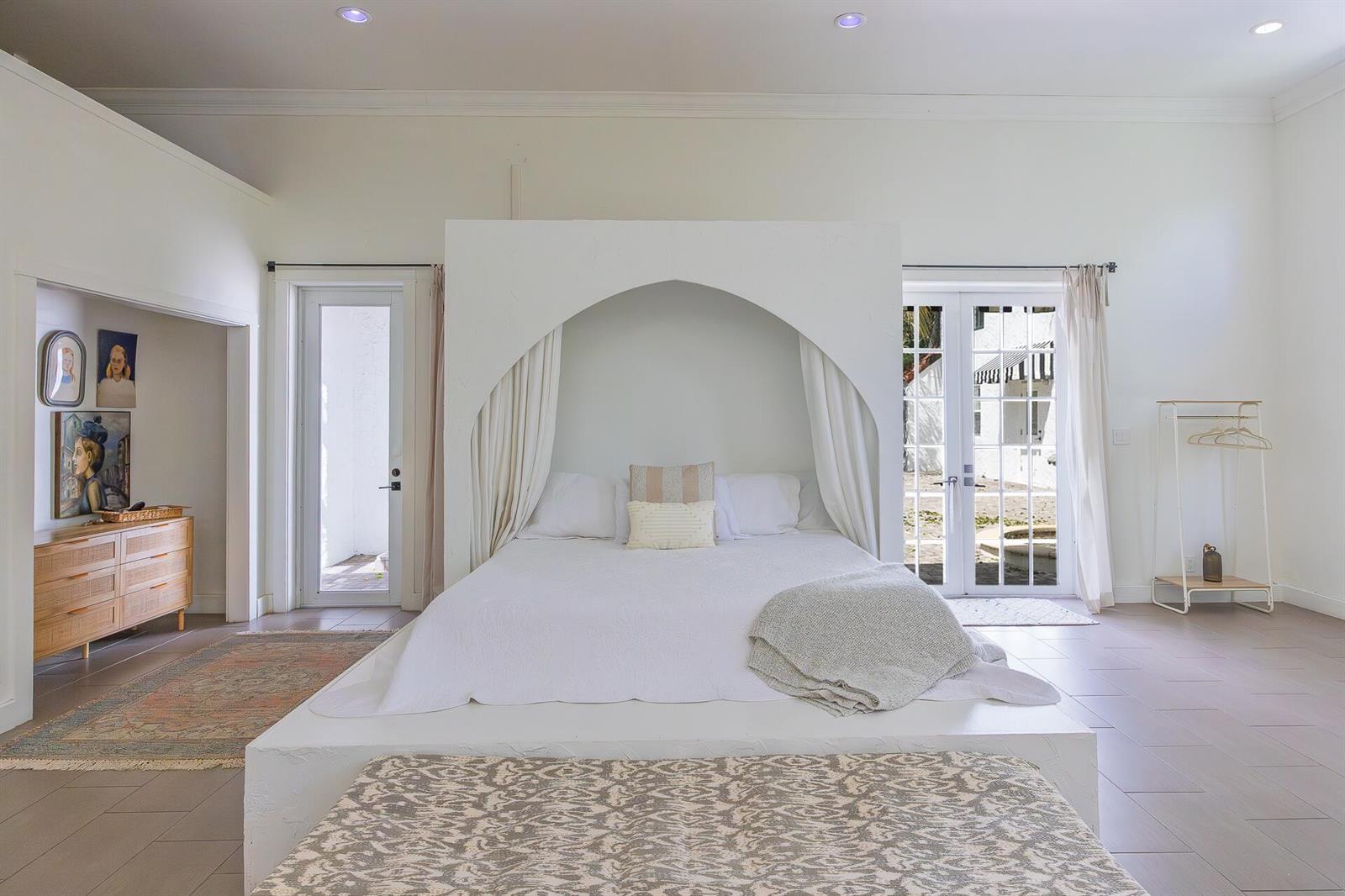 A bedroom features a central arched bed frame, white walls, tile floors, and glass doors — 717 Forest Hill Boulevard, West Palm Beach FL 33405, WEST PALM BEACH, FL
