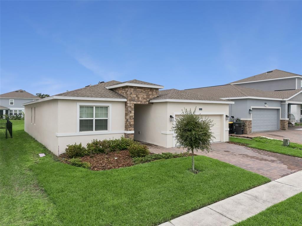 A single-story house with a beige stucco exterior, stone accent wall, and a paved driveway — 4614 WANDSWORTH WAY, DAVENPORT, FL