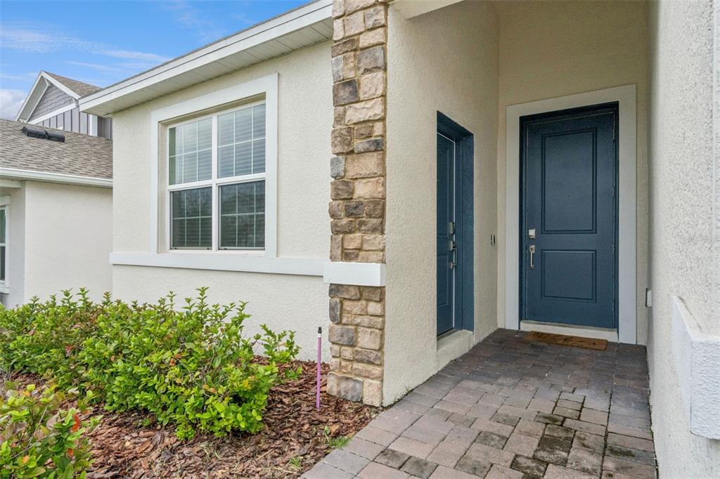 A stone-accented exterior wall features a blue front door and a window above landscaping — 4614 WANDSWORTH WAY, DAVENPORT, FL