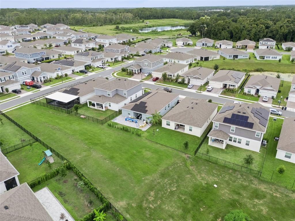 An aerial view shows a suburban neighborhood with houses, fenced backyards, and a nearby pond — 4614 WANDSWORTH WAY, DAVENPORT, FL
