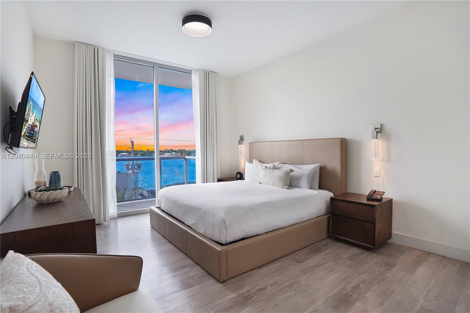 A bedroom features a platform bed, dark wood nightstands, and a balcony overlooking the water — 777 N Ocean Dr # S332, Hollywood FL 33019, HOLLYWOOD, FL