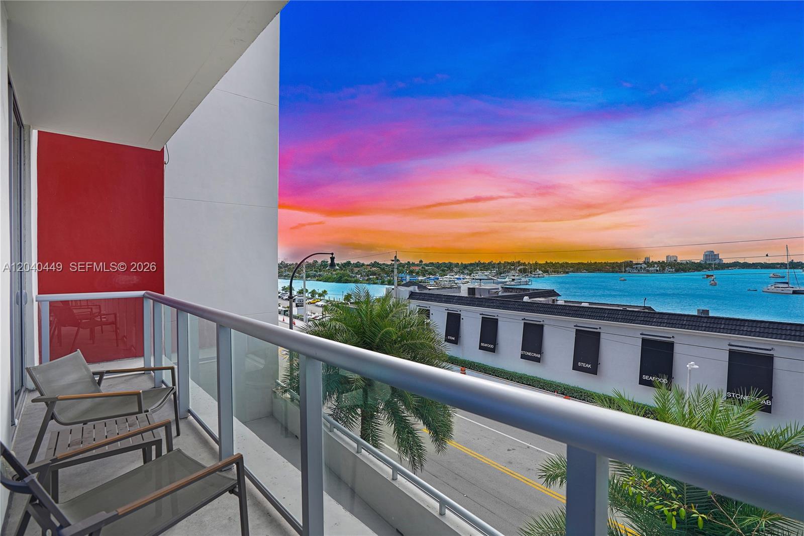A balcony with chairs overlooks a street, a waterfront restaurant, and a vibrant sunset — 777 N Ocean Dr # S332, Hollywood FL 33019, HOLLYWOOD, FL