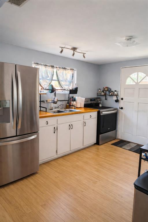 A kitchen features white cabinets, a wood countertop, stainless steel appliances, and light-colored flooring — 2211 SE 51ST STREET, GAINESVILLE, FL