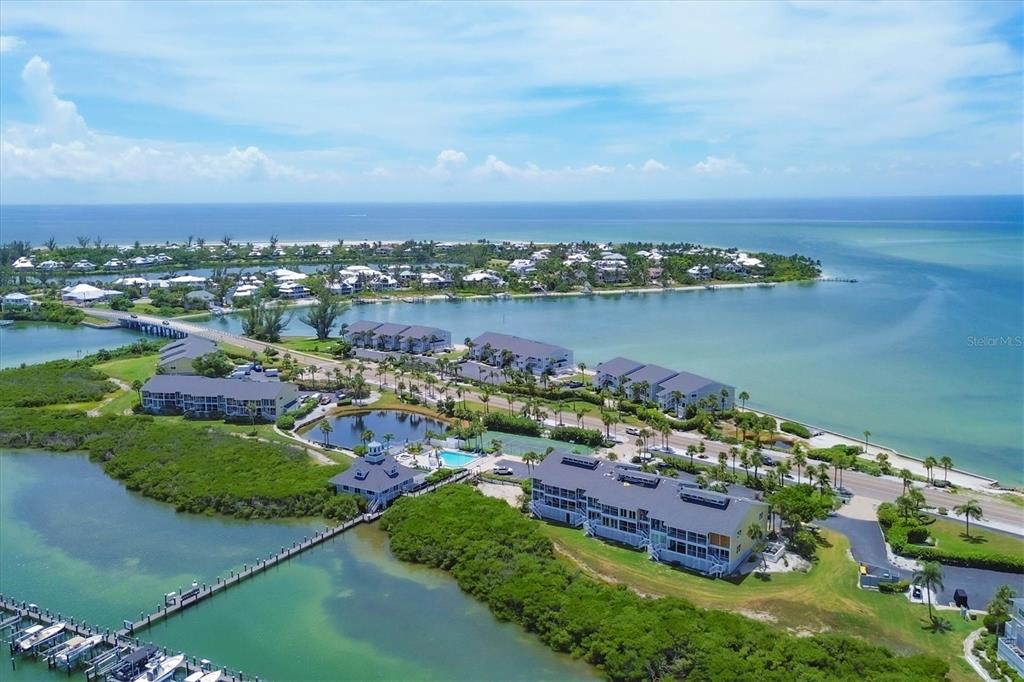 An aerial view shows waterfront condominiums, a boat dock, and a bridge near the ocean — 6001 BOCA GRANDE CAUSEWAY UNIT E58, BOCA GRANDE, FL