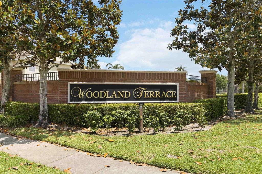 A brick entrance monument with a sign reading Woodland Terrace stands among trees and landscaping — 534 TERRACE SPRING DRIVE, ORLANDO, FL