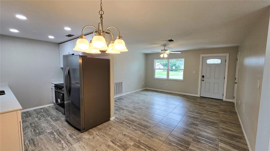 A kitchen and dining area feature light-colored walls, tile flooring, and a stainless steel refrigerator — 115 PADGETT PLACE S, LAKELAND, FL