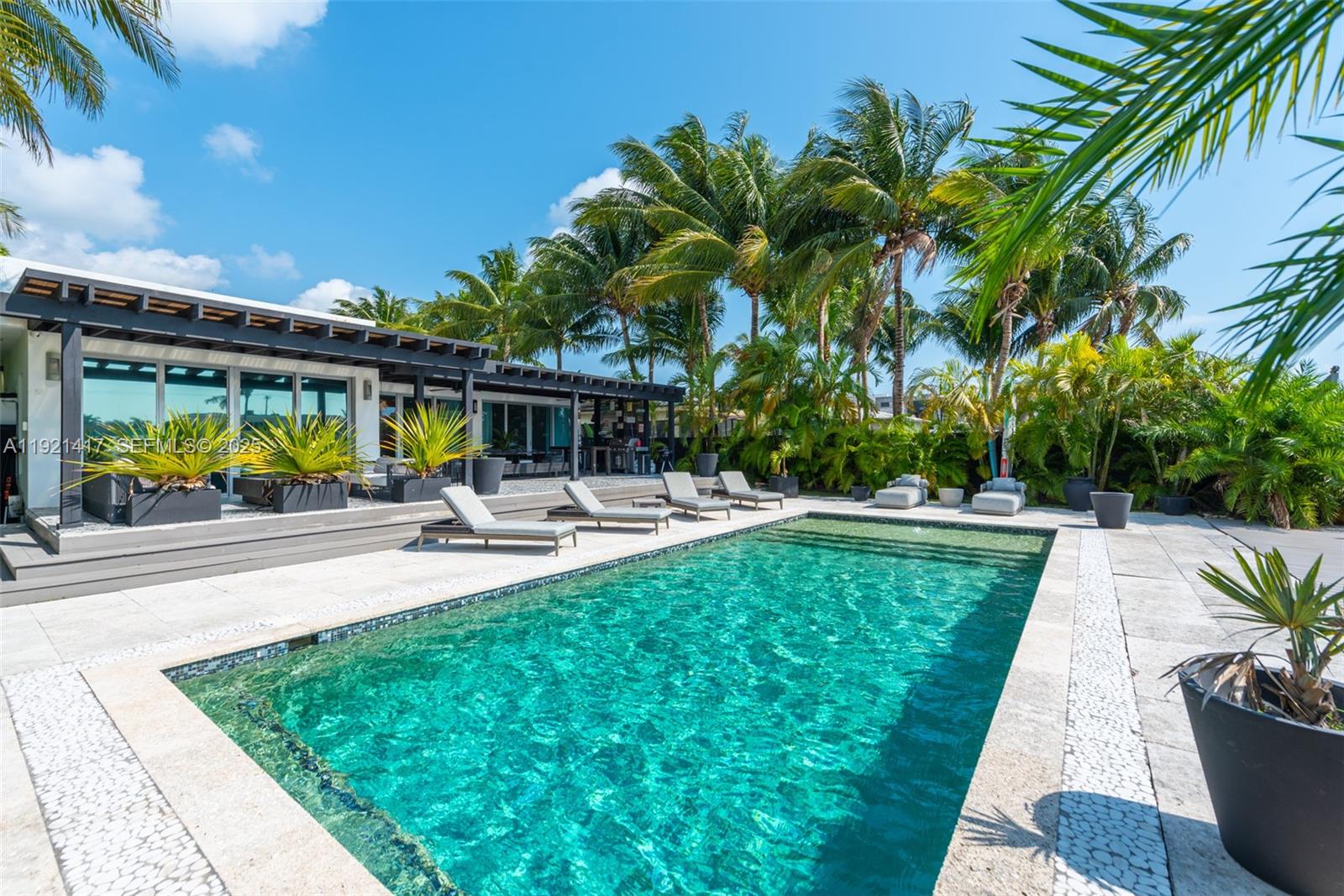 A swimming pool sits on a stone patio beside a modern house with palm trees — 970 S Shore Dr, Miami Beach FL 33141, MIAMI BEACH, FL