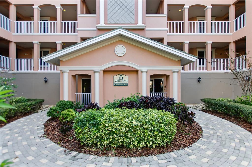 A paved walkway leads to the entrance of a multi-story peach-colored apartment building — 5209 MANORWOOD DRIVE UNIT 3A, SARASOTA, FL