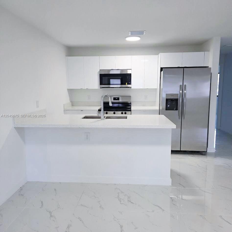 A modern kitchen features white cabinets, stainless steel appliances, and a white quartz breakfast bar — 2731 NW 44th St # 2731, Miami FL 33142, MIAMI, FL