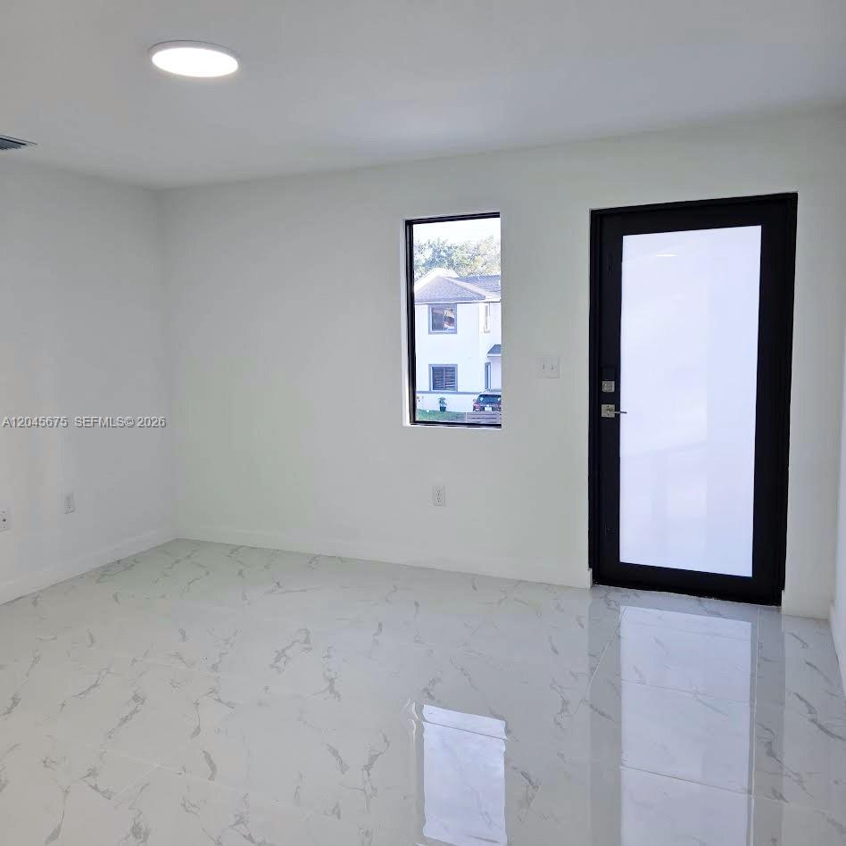 A minimalist room features white walls, marble-patterned tile flooring, a single window, and a door — 2731 NW 44th St # 2731, Miami FL 33142, MIAMI, FL