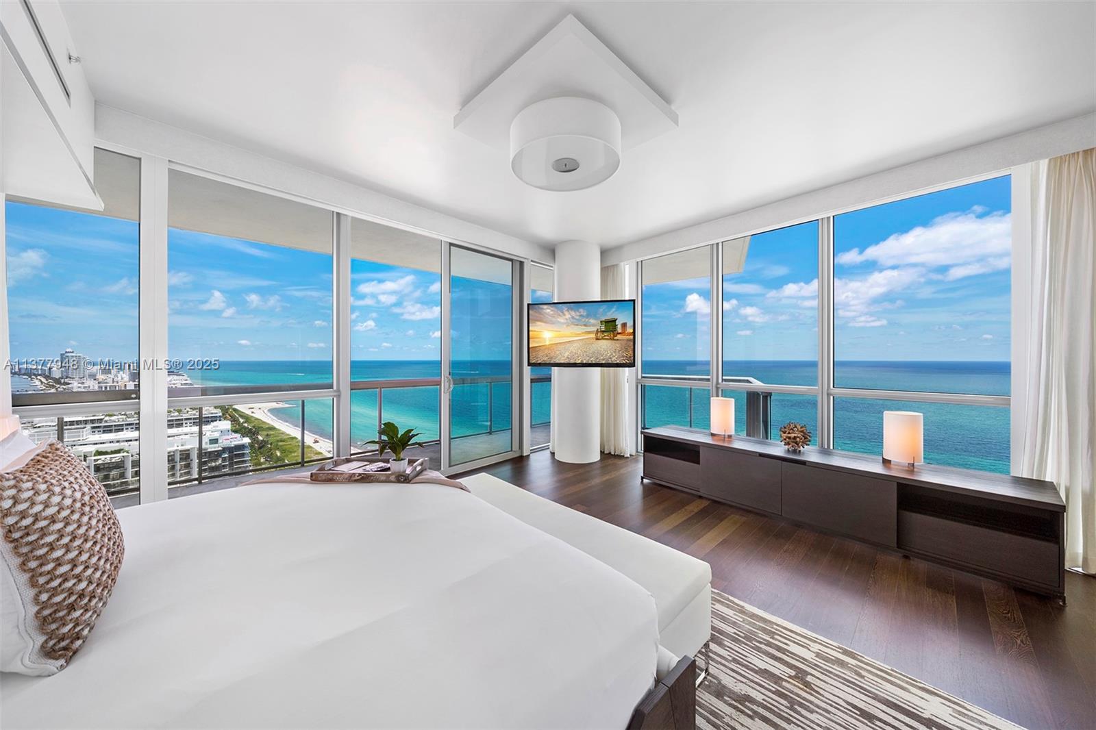 A modern bedroom features floor-to-ceiling windows with ocean views, a mounted television, and dark wood flooring — 101 20th St # 3909, Miami Beach FL 33139, MIAMI BEACH, FL