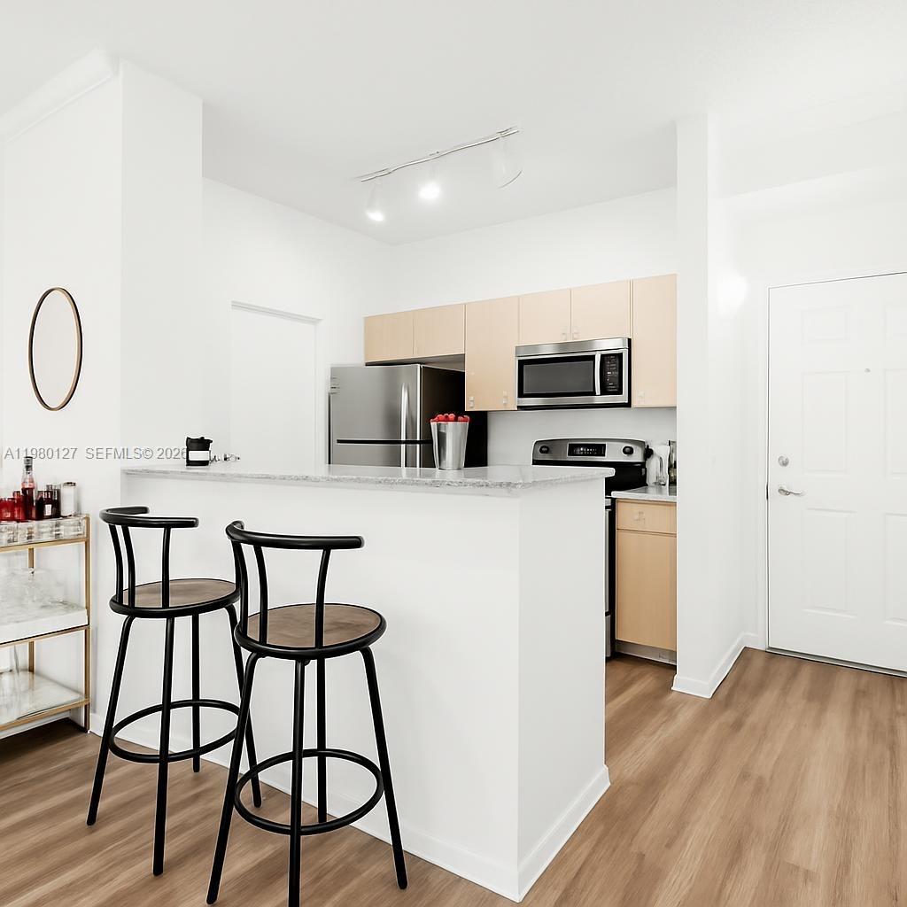 A kitchen features light wood cabinets, stainless steel appliances, and a breakfast bar with stools — 1900 Van Buren St # 112B, Hollywood FL 33020, HOLLYWOOD, FL