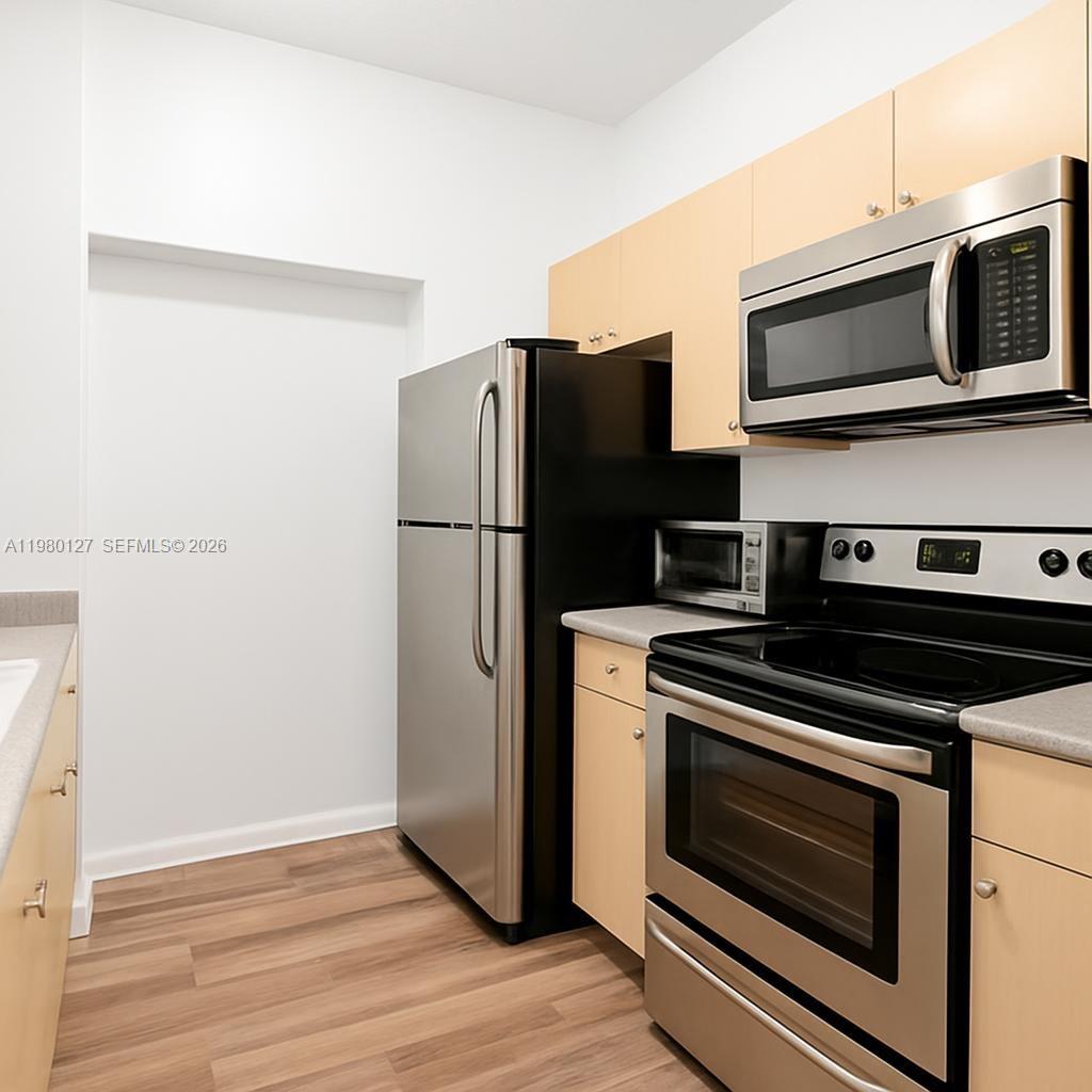 A kitchen features light wood cabinets, stainless steel appliances, and wood-look flooring — 1900 Van Buren St # 112B, Hollywood FL 33020, HOLLYWOOD, FL