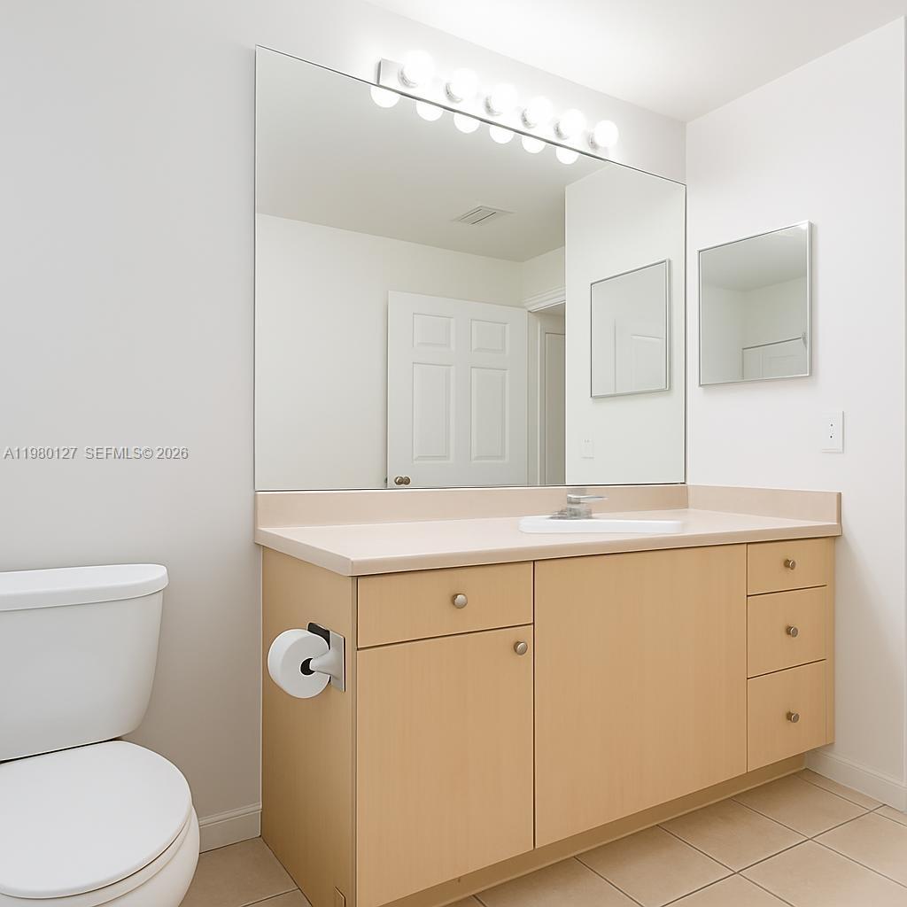 A bathroom features a light wood vanity, a large wall mirror, and a toilet — 1900 Van Buren St # 112B, Hollywood FL 33020, HOLLYWOOD, FL