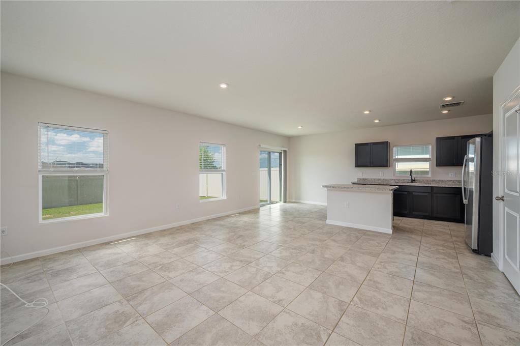 An open-concept living area with tile flooring, a kitchen with dark cabinets, and sliding doors — 166 PIAVE STREET, HAINES CITY, FL