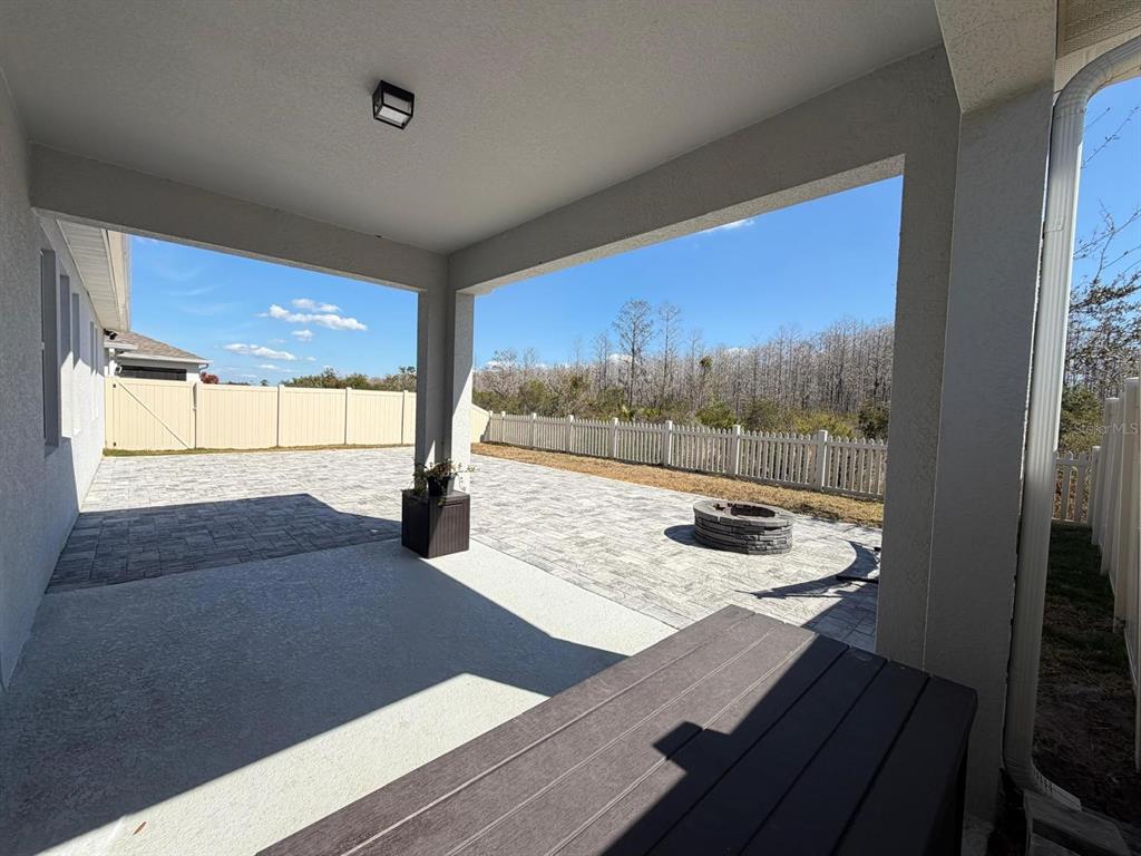 A covered patio features a paved floor, a fire pit, and a white vinyl fence — 3647 VEGA CREEK DRIVE, ST CLOUD, FL