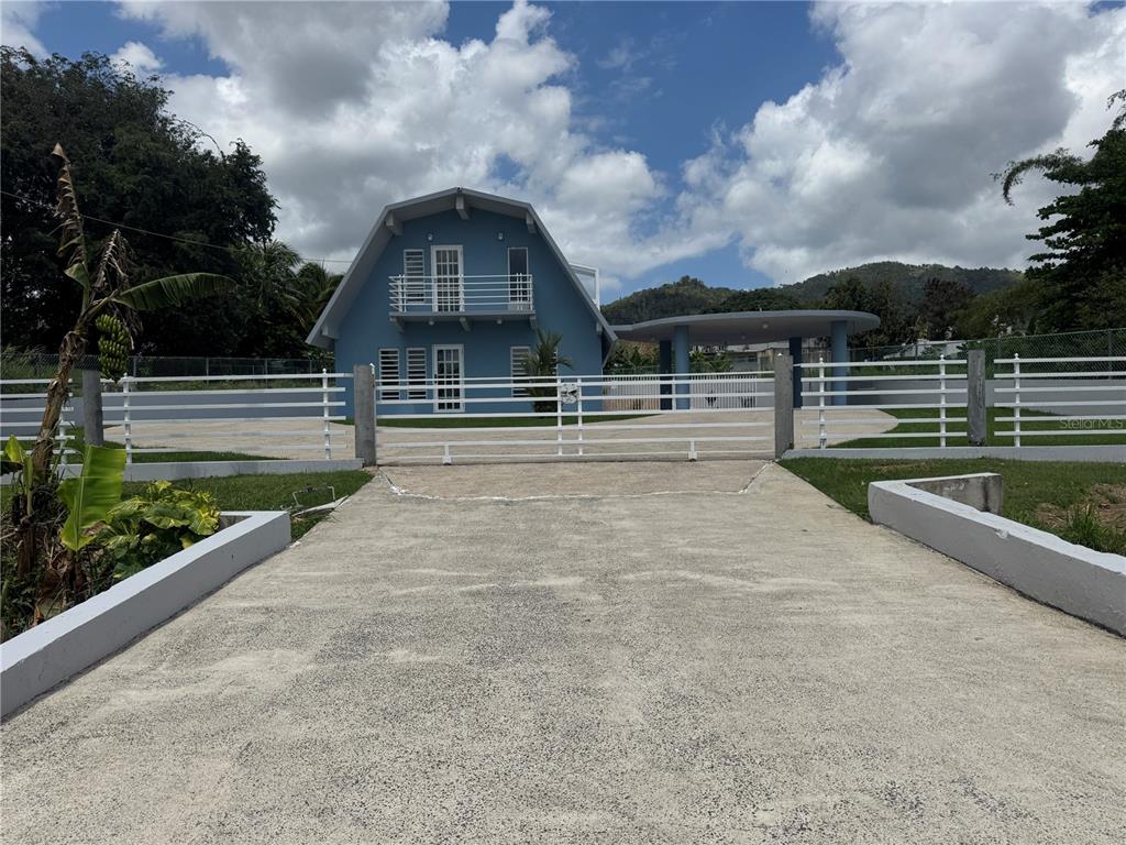 A blue, gambrel-roofed house with a balcony and circular carport sits behind a white fence — 5 BO CELADA, GURABO, PR