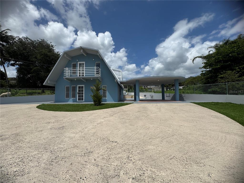 A blue A-frame house features a balcony, a large circular carport, and a paved driveway — 5 BO CELADA, GURABO, PR