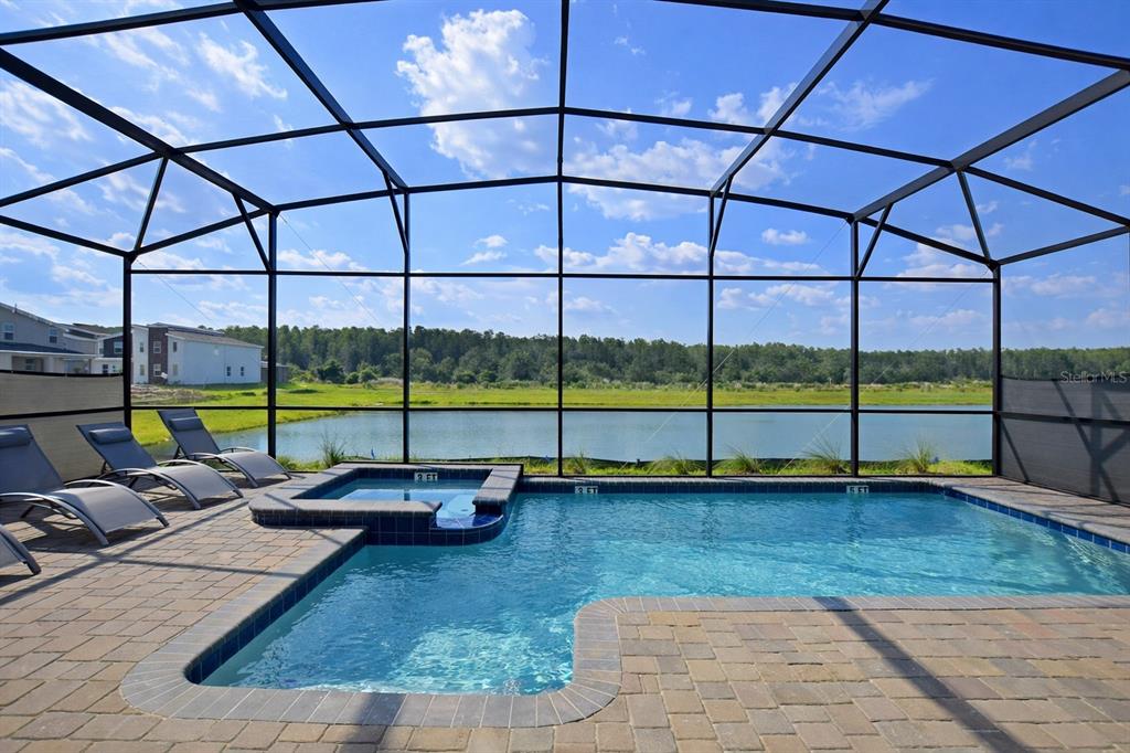 A screened-in patio features a swimming pool and spa overlooking a pond and trees — 4213 PARAGRAPH DRIVE, KISSIMMEE, FL