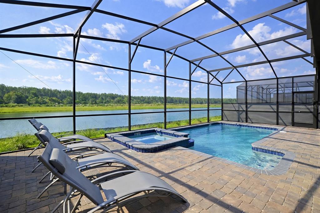 A screened-in pool and spa area with lounge chairs overlooking a lake and forest — 4213 PARAGRAPH DRIVE, KISSIMMEE, FL