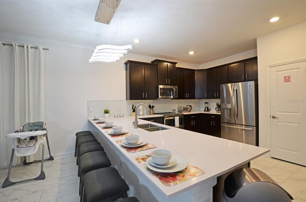A kitchen features dark wood cabinets, a large white island with seating, and stainless appliances — 4213 PARAGRAPH DRIVE, KISSIMMEE, FL