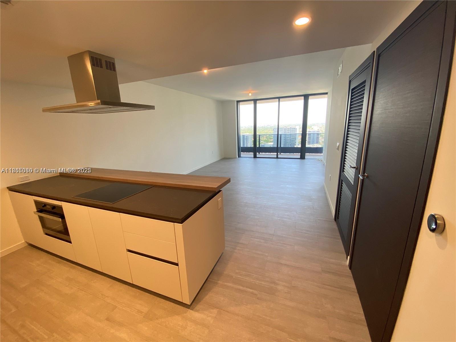 A kitchen island with a cooktop and range faces an open living area with floor-to-ceiling windows — 1000 Brickell Plz # 3010, Miami FL 33131, MIAMI, FL