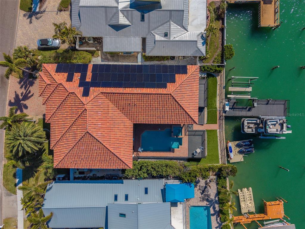 An aerial view shows a waterfront home with a tiled roof, solar panels, and a pool — 824 ISLAND WAY, CLEARWATER BEACH, FL