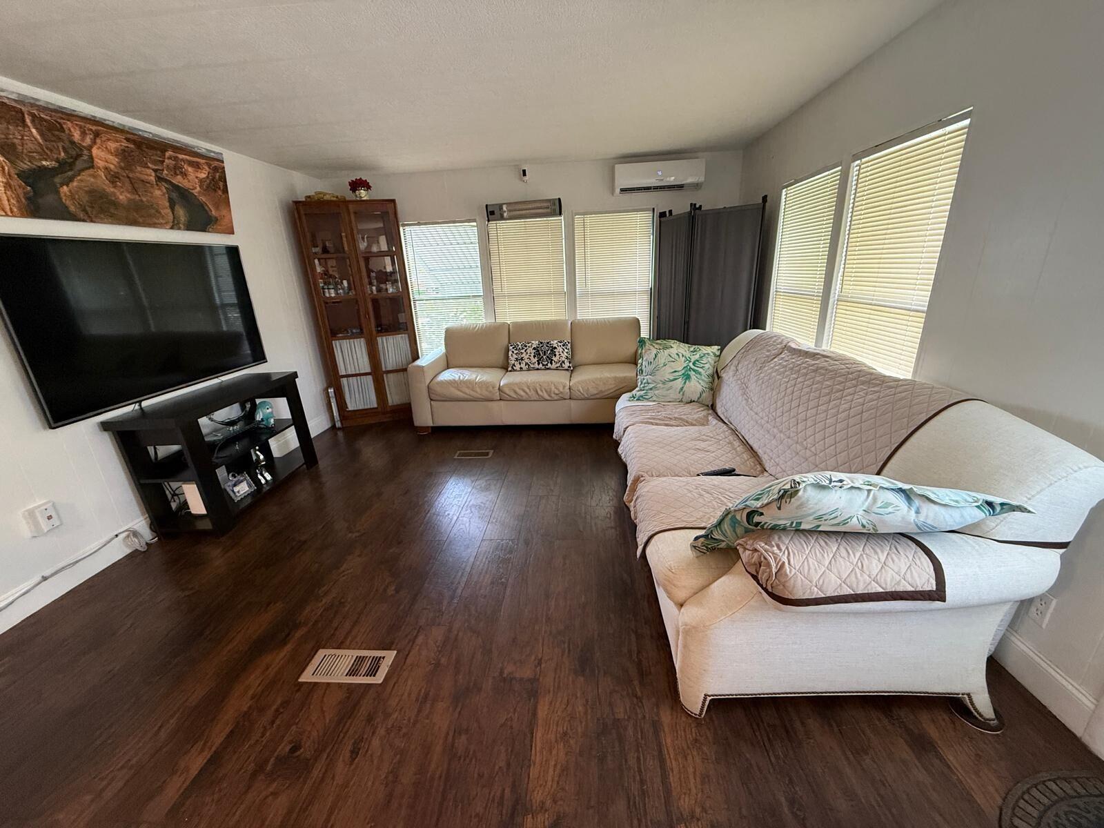 A living room features dark wood flooring, a television, two sofas, and a wooden cabinet — 3875 Sheraton Circle # 121, Boynton Beach FL 33436, BOYNTON BEACH, FL
