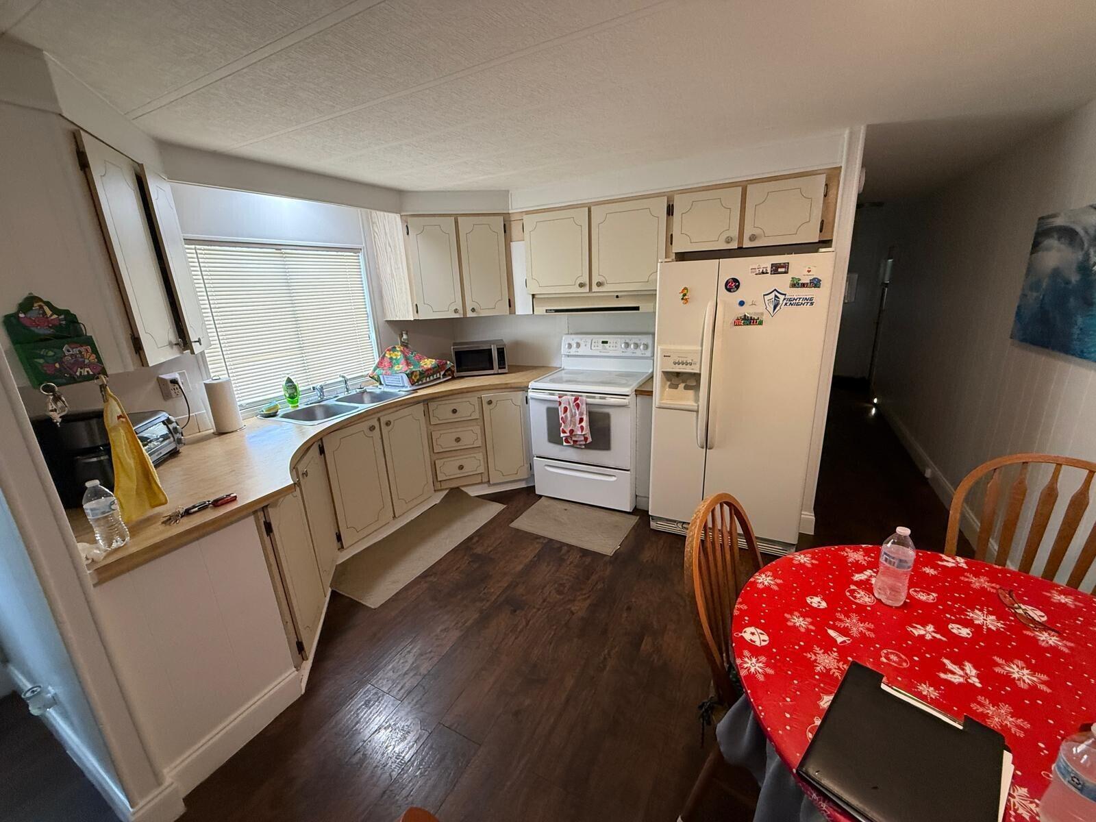 A kitchen with light-colored cabinets, white appliances, wood-look flooring, and a round dining table — 3875 Sheraton Circle # 121, Boynton Beach FL 33436, BOYNTON BEACH, FL